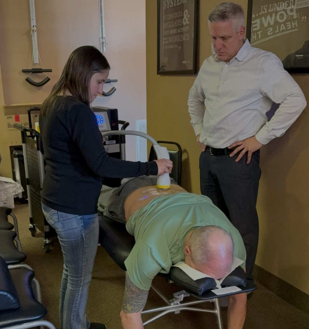 Dr. Chris Hansen supervising a SoftWave therapy session as a staff member treats a patient's lower back at Hansen Chiropractic
